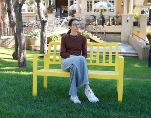 A woman is sitting on a yellow bench gazing into the distance