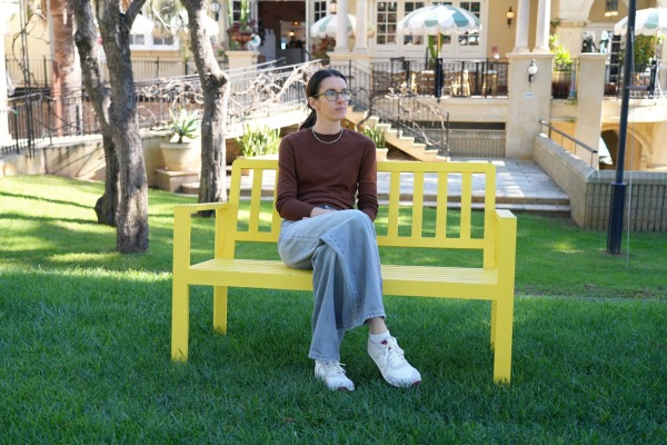 A woman is sitting on a yellow bench gazing into the distance