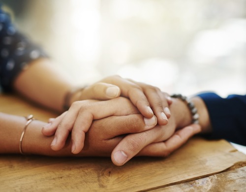 A person holding another person's hand with both their hands in a comforting manner