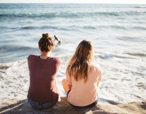 Two people sitting on a rock with their backs visible facing the ocean