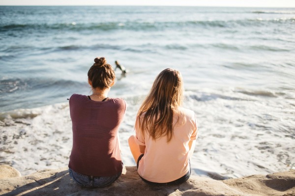 Two people sitting on a rock with their backs visible facing the ocean