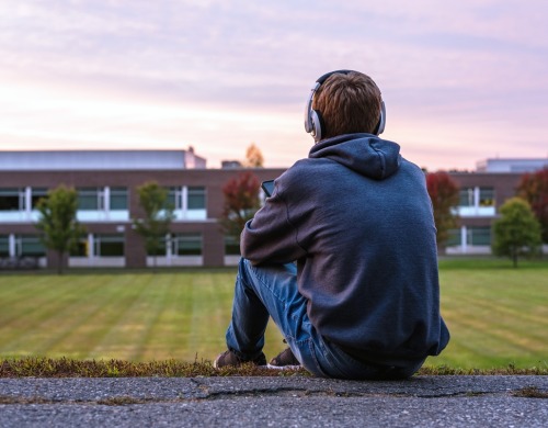 A person sitting facing a field with headphones on