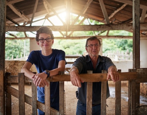 A father and son in a barn leaning against a fence smiling