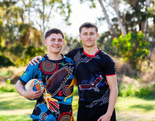 Two young male rugby players smiling, with one resting his arm on the other's shoulder
