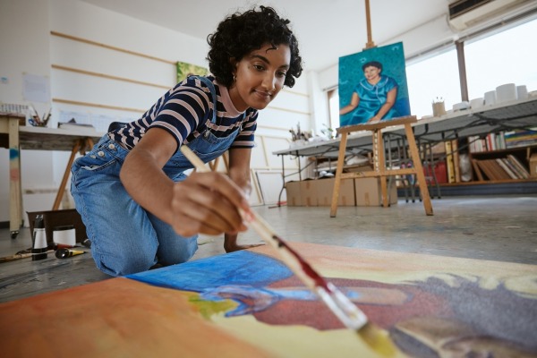 Art studio with a woman painting on a canvas on the floor.