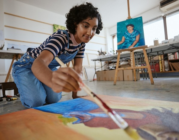Art studio with a woman painting on a canvas on the floor.