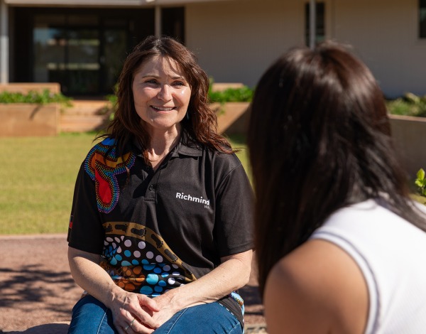A Richmind WA worker talking to another person, both sitting on rocks outside in a garden