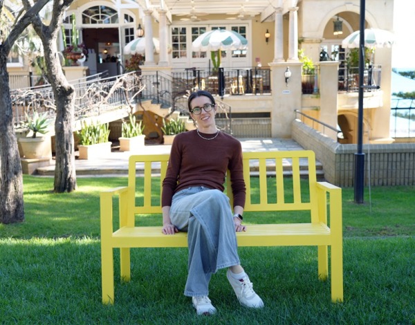 Woman sitting on a yellow bench smiling, in a park